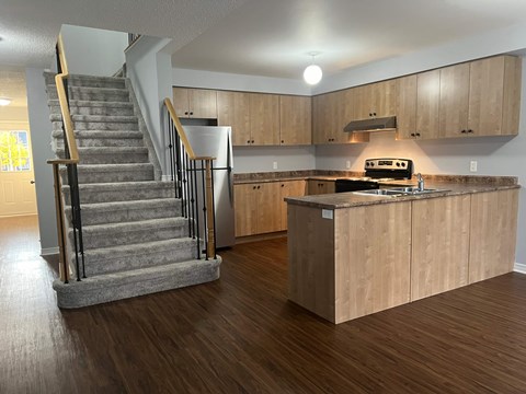 A kitchen with wooden cabinets and a staircase with a metal railing.