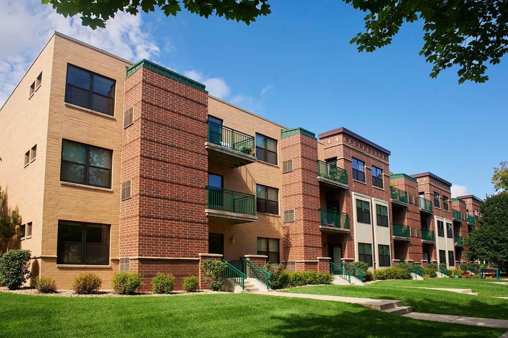 A large brick apartment building with balconies and a green lawn in front.