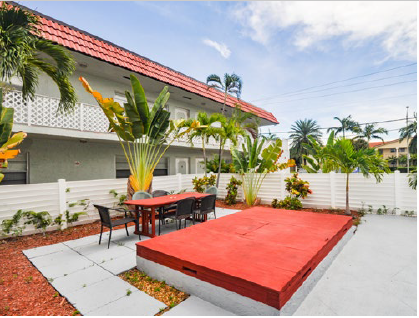 a patio with a red table and chairs in front of a house