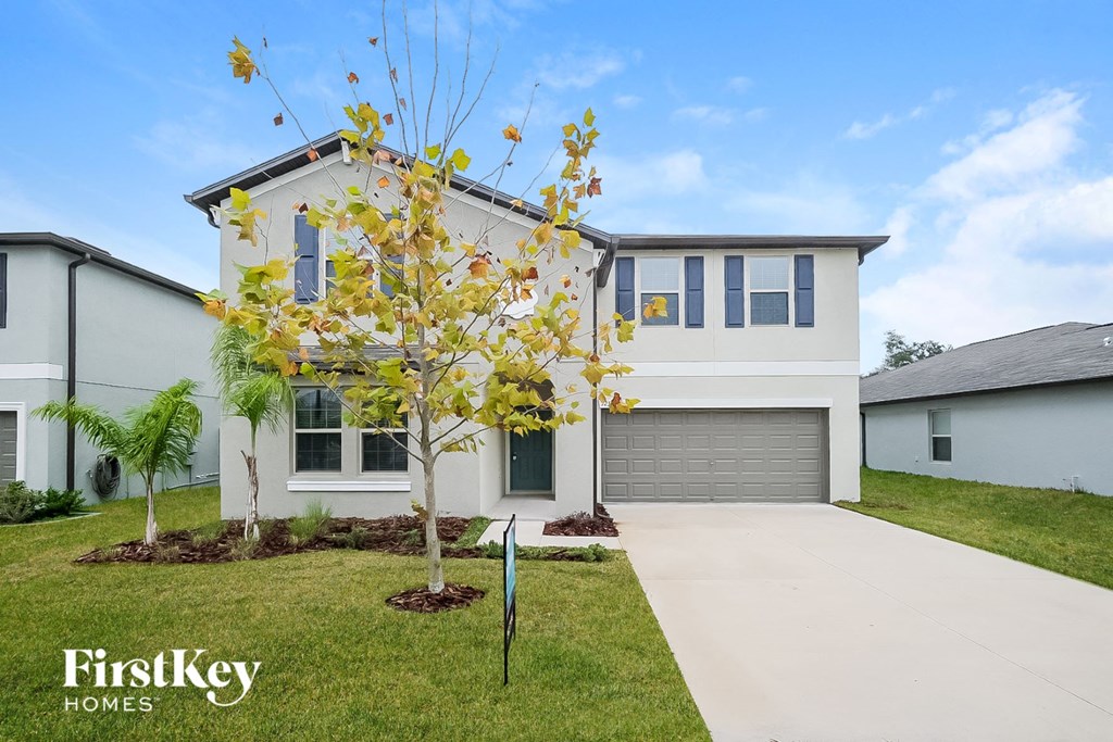 a white house with a driveway and a tree in front of it