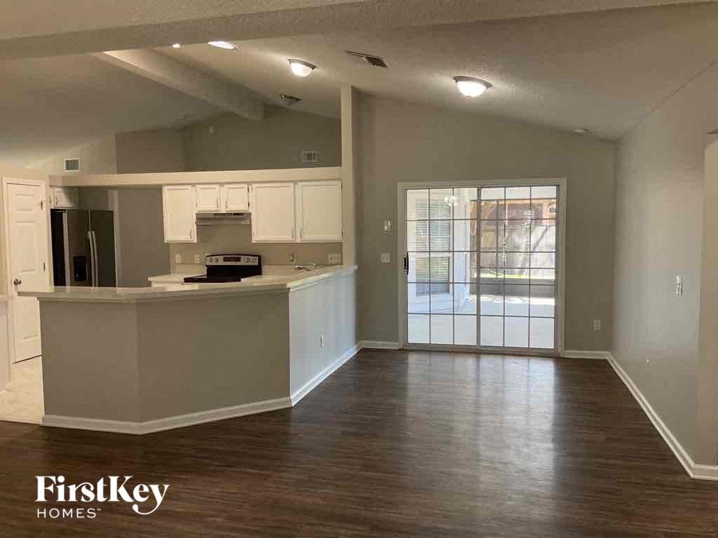 an empty living room with a kitchen and a door to a patio