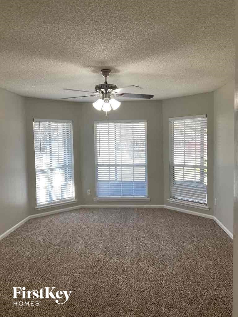 an empty living room with a ceiling fan and three windows