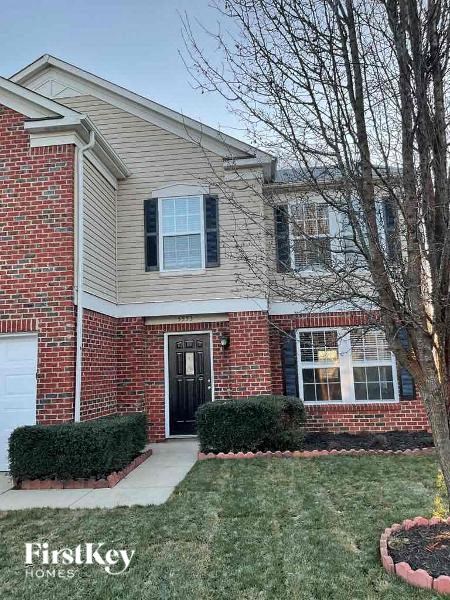the front of a brick house with a lawn and a tree