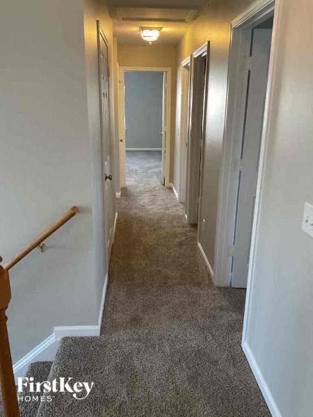 A hallway with a carpeted floor and a staircase on the left side.