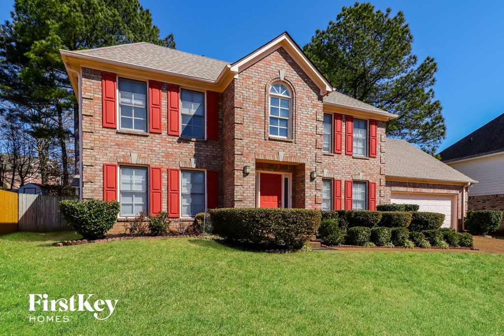 a brick house with red shuttered windows and a lawn