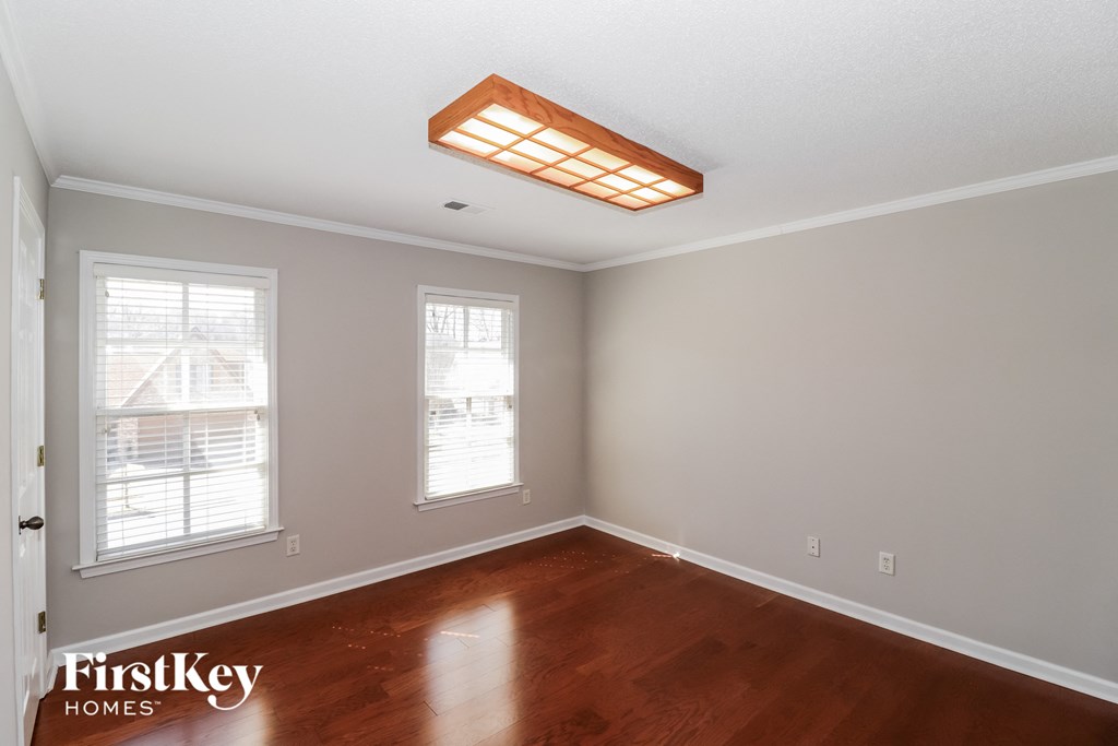 a bedroom with a wood floor and a ceiling light and two windows