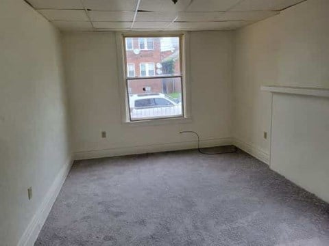 A room with a window and a view of a street and buildings outside.