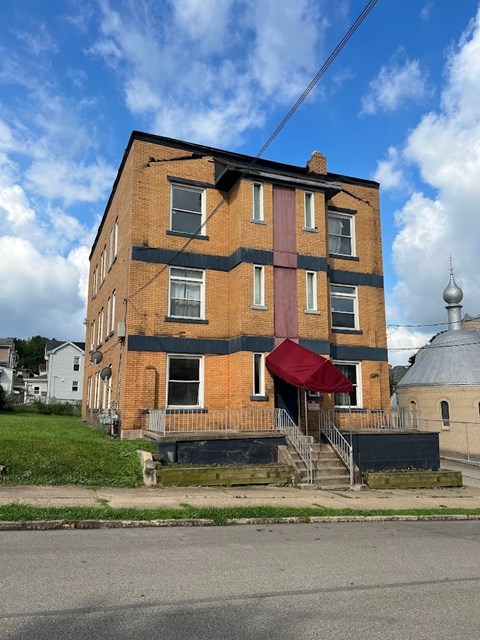 A red awning is on the front porch of a brick building.