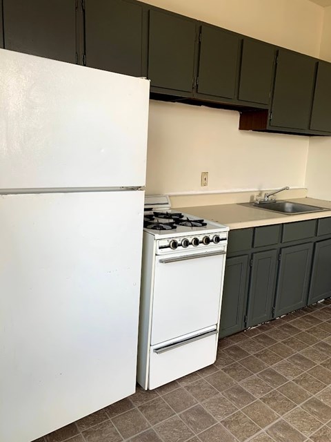 A white refrigerator is in a kitchen with a white stove and green cabinets.