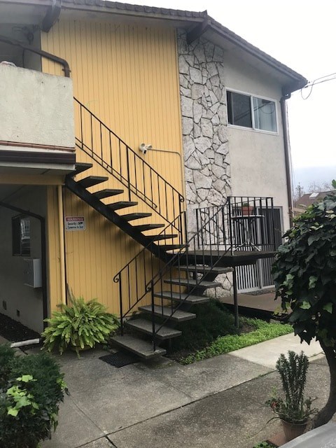 A yellow house with a stone wall and a black metal staircase.