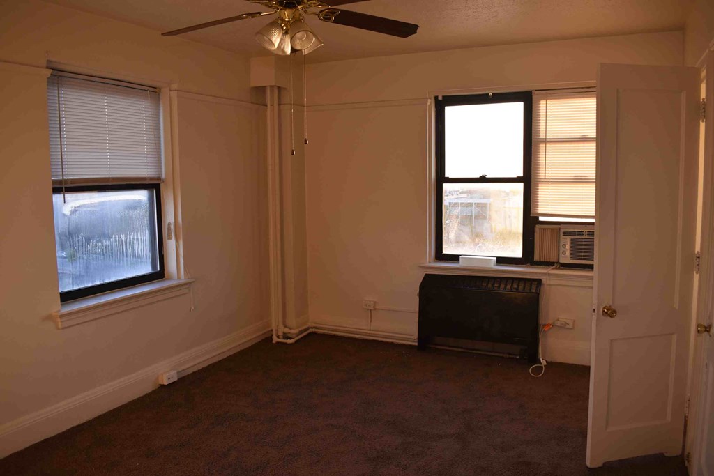 an empty living room with a ceiling fan and two windows