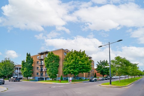 A street view of a residential area with apartment buildings and parked cars.
