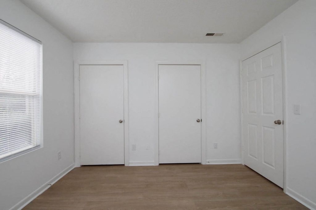 a bedroom with white walls and a wood floor and two doors