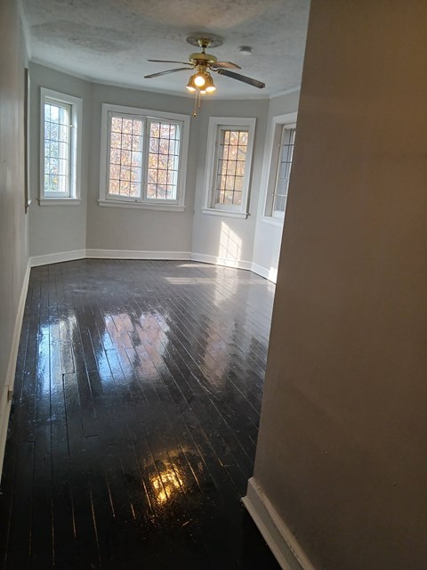 A room with a ceiling fan and three windows.