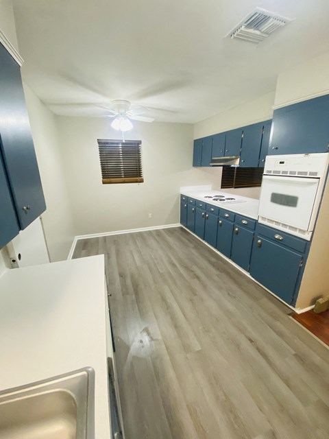 a kitchen with blue cabinets and white appliances and wood flooring