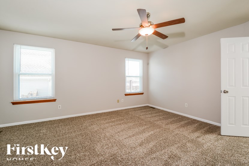 A room with a carpet floor, a ceiling fan, and a door.