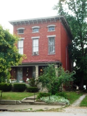 A red brick house with a porch and a small garden in front.