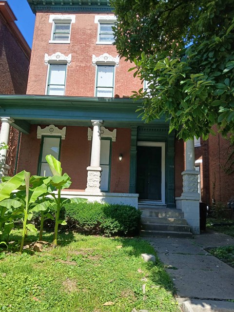 the front of a brick house with a green porch