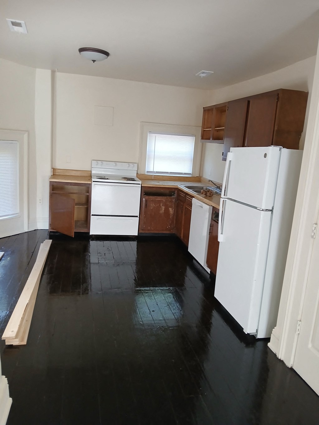 an empty kitchen with white appliances and wooden floors