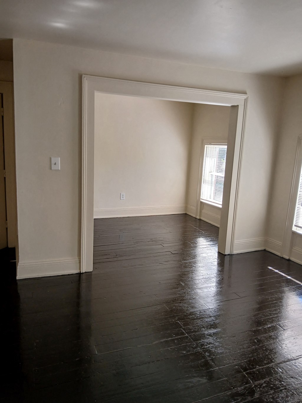 an empty living room with dark wood floors and white walls