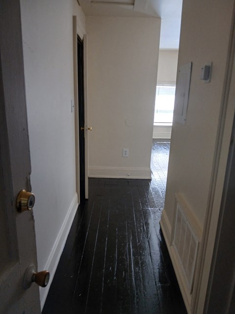 a hallway with wood floors and white walls and an open door