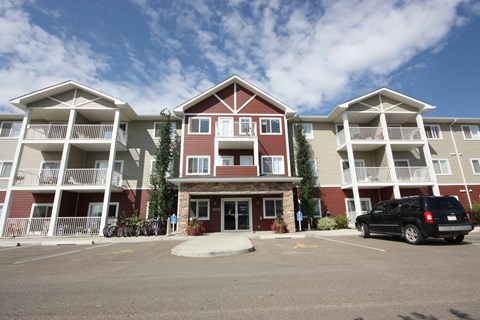 A black car is parked in the parking lot of a three-story apartment building.