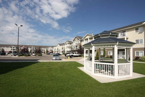 A white gazebo is in the middle of a grassy area in front of apartment buildings.