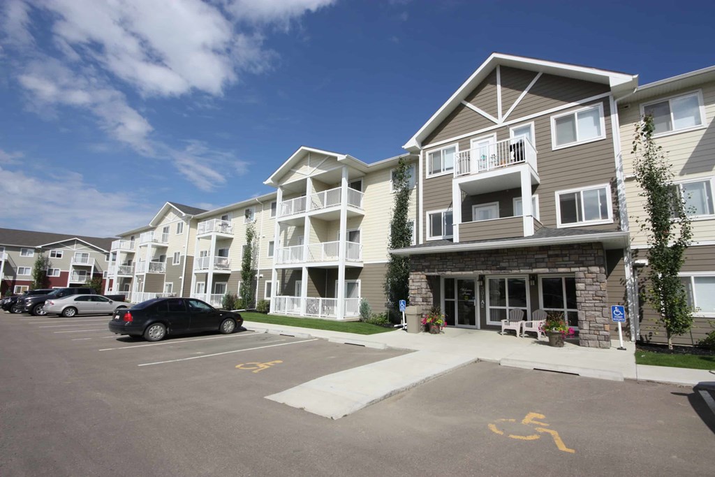A parking lot in front of a building with a car parked in the spot with a wheelchair symbol.
