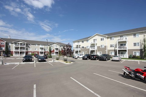 A parking lot with cars and motorcycles in front of apartment buildings.