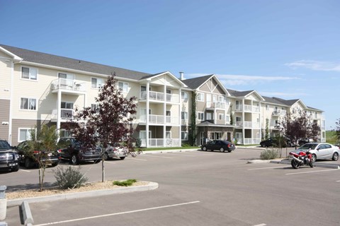 A parking lot in front of apartment buildings with cars parked.