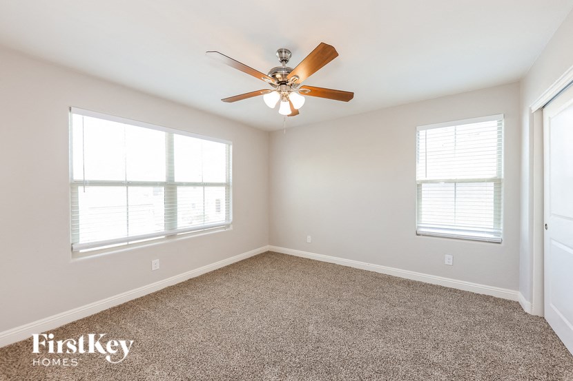 A room with a ceiling fan and two windows.