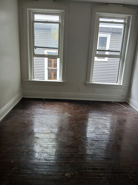 an empty room with two windows and wood floors
