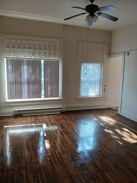 an empty living room with a ceiling fan and two windows
