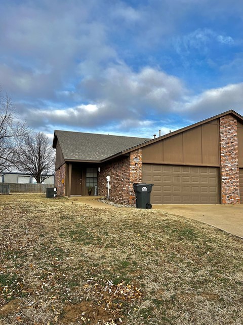 a brick house with a brown garage and a cloudy sky