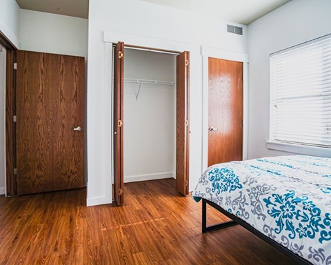 A bedroom with a bed, wooden closet doors, and a window with blinds.