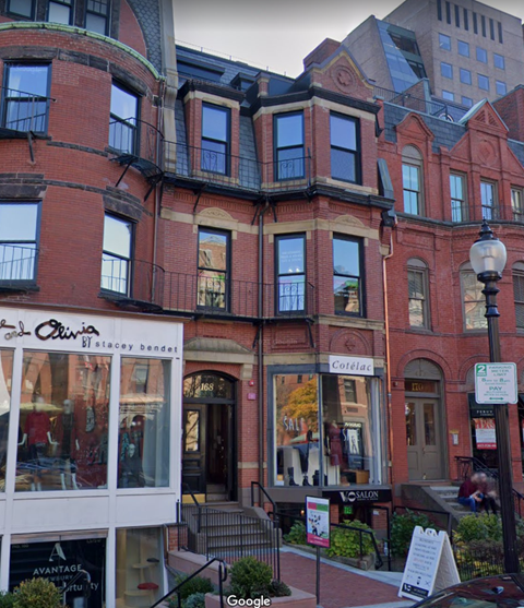 A street view of a red brick building with a storefront on the ground floor.