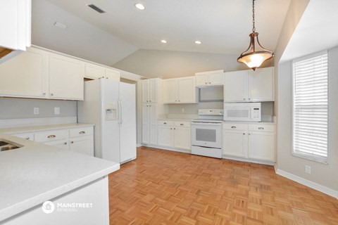 an open kitchen with white cabinets and white appliances and a wooden floor