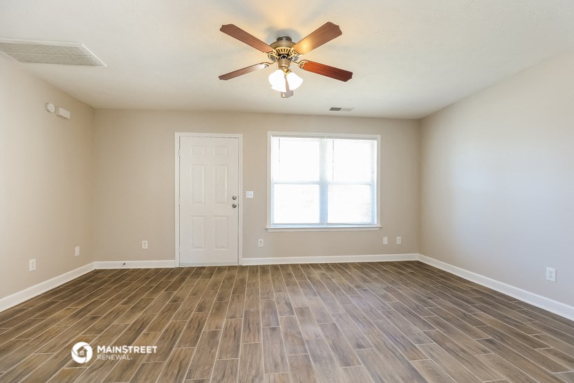 the spacious living room with wood flooring and a ceiling fan