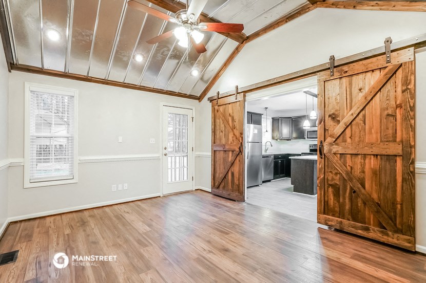 an empty living room with wooden sliding barn doors and a kitchen