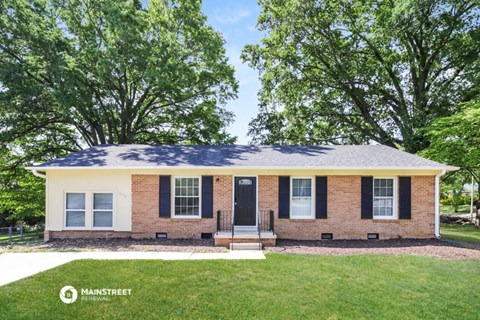 a small brick house with black shutters and a front yard