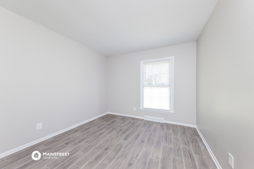 a bedroom with white walls and wood floors and a window