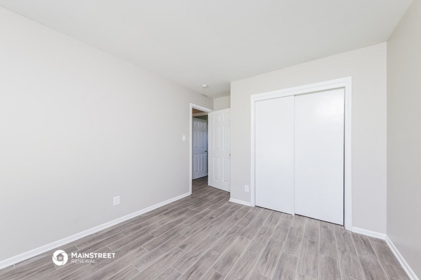 a bedroom with white walls and wood flooring and a closet