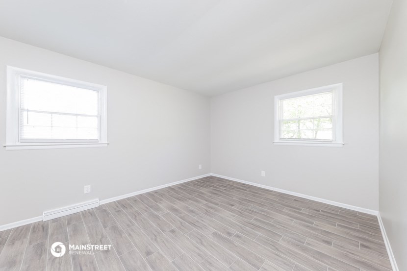 an empty room with wood floors and two windows