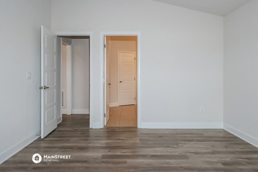 a bedroom with white walls and wood flooring and a door to a closet