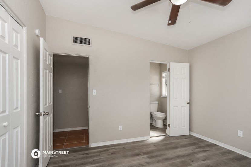 a bedroom with a door to the bathroom and a ceiling fan