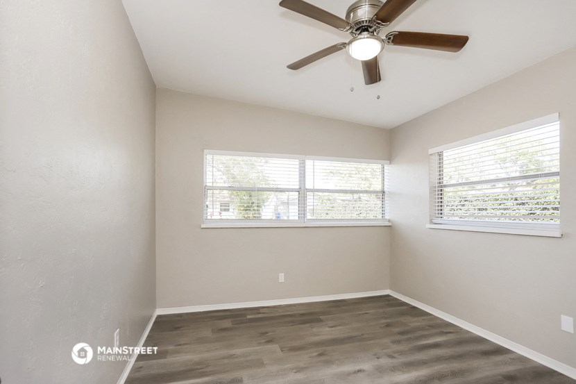 an empty room with a ceiling fan and two windows