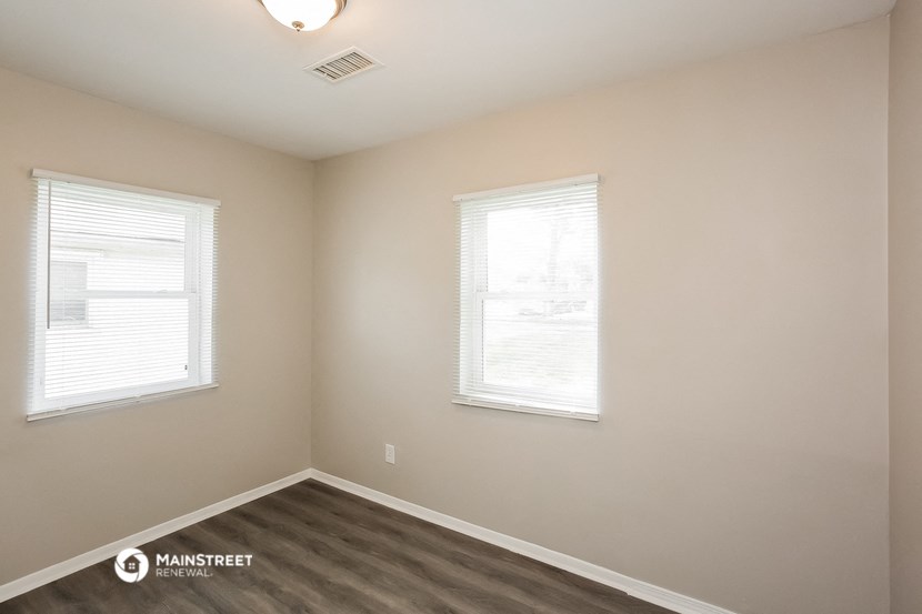 the interior of an empty room with wood flooring and two windows