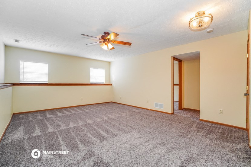 the living room is spacious with carpet and a ceiling fan