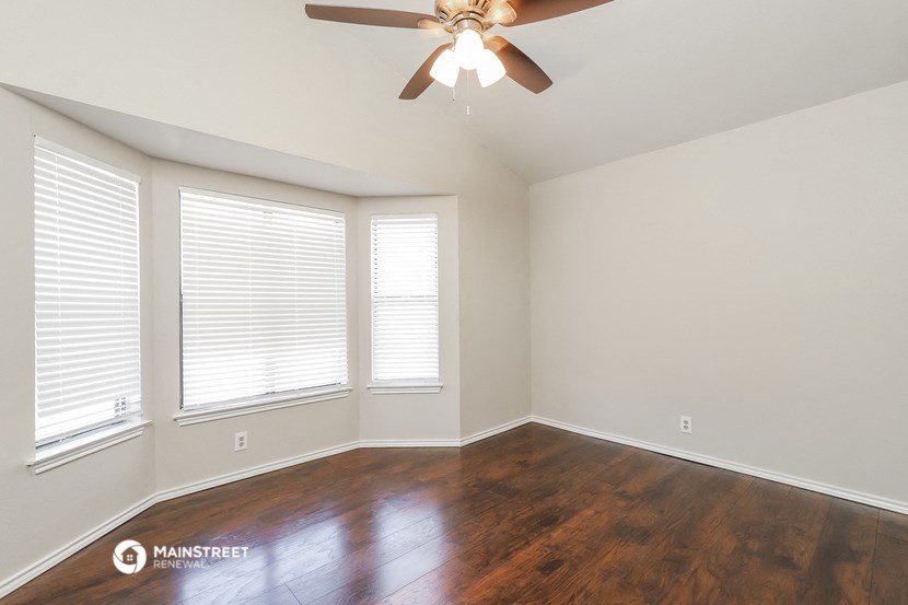 the spacious living room with wood floors and a ceiling fan