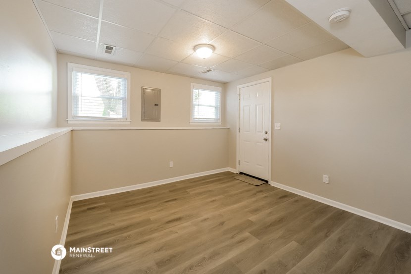 the living room of an empty home with wood flooring and a white door